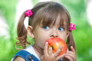 Little girl portrait eating red apple outdoor